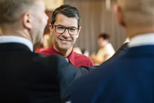 Portrait of Victor Nazareth with the backs of two men in the foreground. Photo.